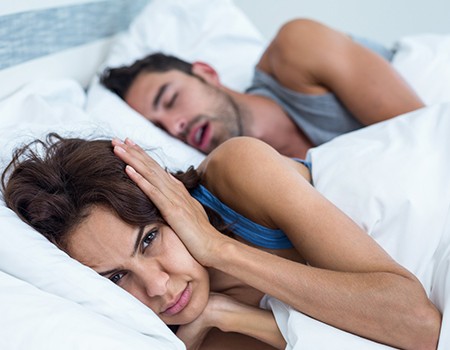 Woman covering her ears while husband snores