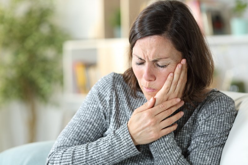 Woman on couch with jaw pain from TMJ disorder