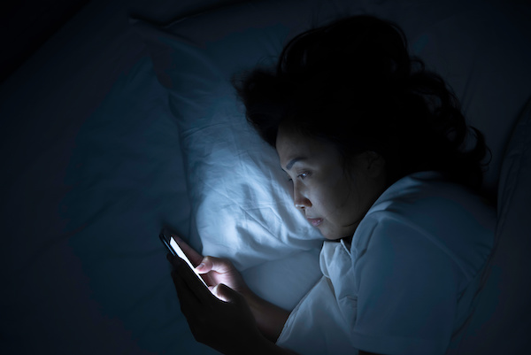 sleepless woman in bed looking at phone
