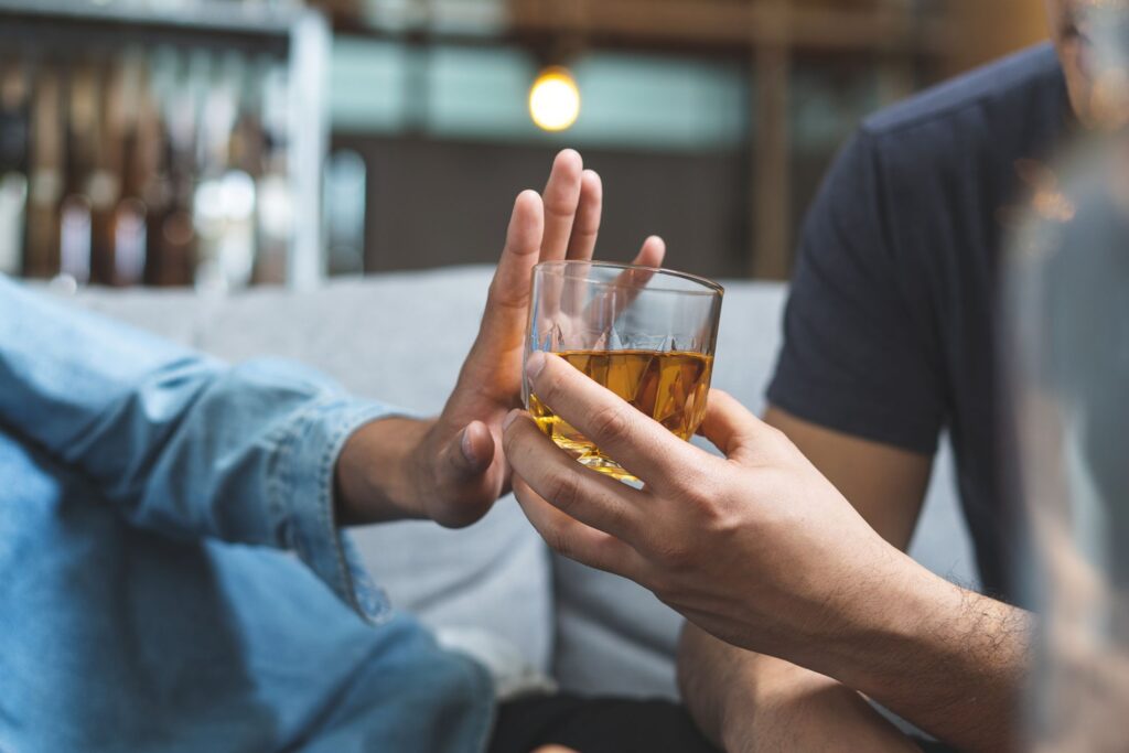 One hand turning down an alcoholic drink offered by another